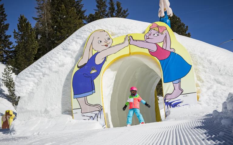Ein Kind auf Ski fährt durch einen kurzen Tunnel im KidsSlope