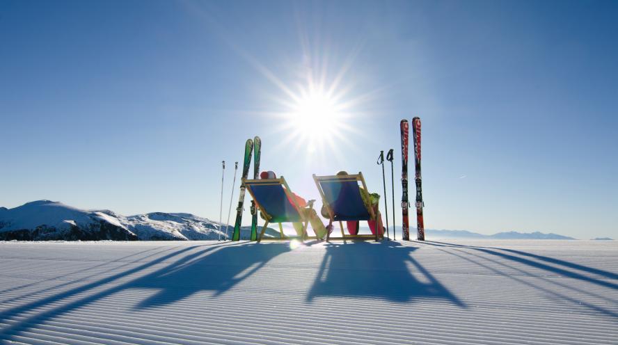Zwei Skifahrer machen Pause und nutzen die Liegestühle die an den Pisten aufgestellt wurden. Ein Service der Region Turracher Höhe. Pisten-Liegestuhl